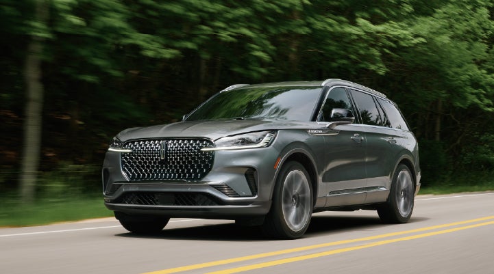 A 2027 Lincoln Aviator® SUV is being driven down a road lined with trees. | Dutch Miller Lincoln of Ashland in Ashland KY